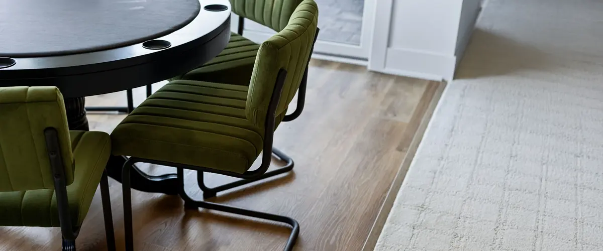 A close-up of a table with stylish green velvet chairs and wooden flooring in a game room.