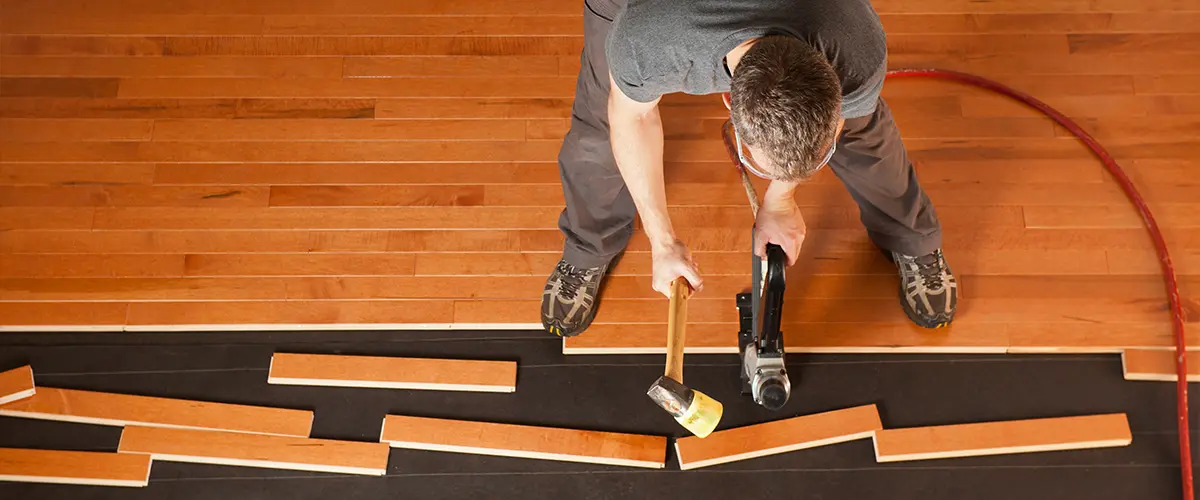 A contractor installing hardwood flooring using a mallet and nailer for precision.