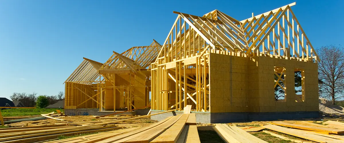 New home construction with wooden framing in progress, showing roof trusses and building materials on-site.