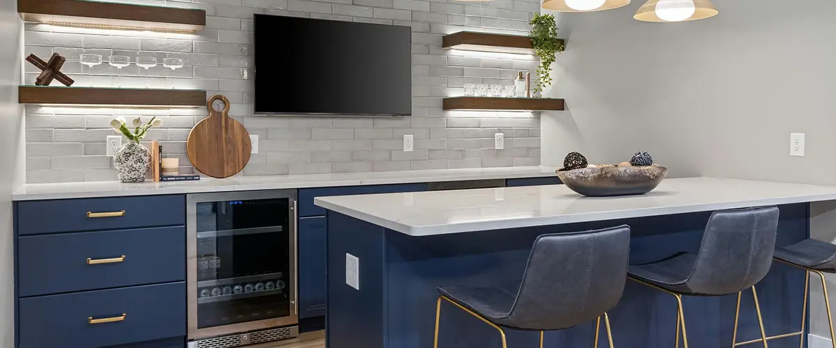 Stylish home bar with navy blue cabinets, gold accents, pendant lighting, and floating shelves with LED lighting.