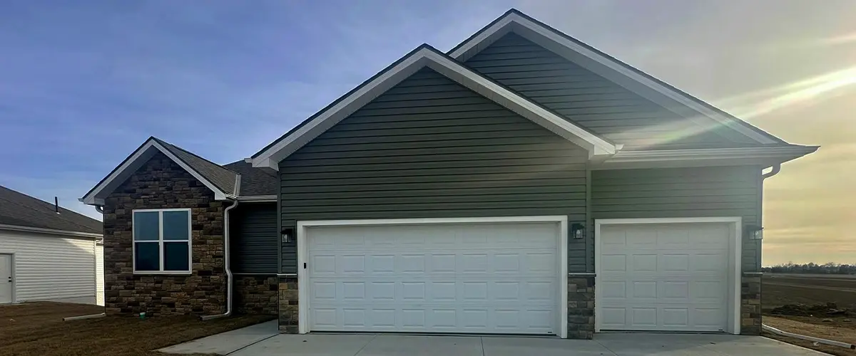 Modern suburban home with green siding and three-car garage on concrete driveway under blue sky